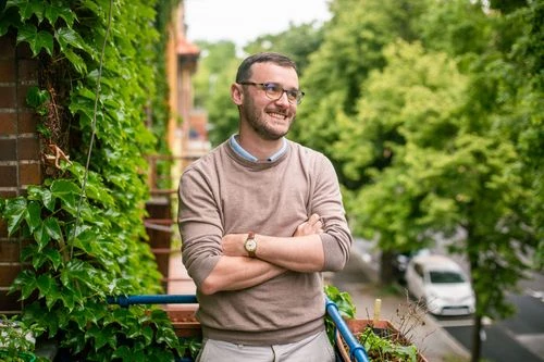 Muž stojí na balkóně v Praze s výhledem do ulice.