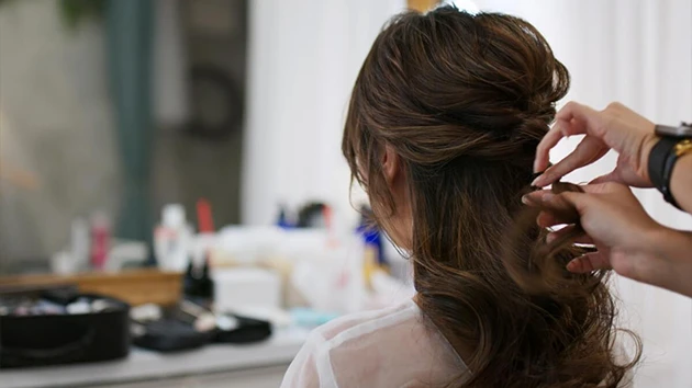 Stylista upravuje nevěstiny vlasy do svatebního účesu.